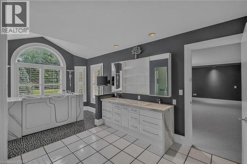 Spacious bathroom featuring a white walk-in tub with marble-look surround, an arched window with plantation shutters, a double vanity with stone countertops, and contrasting white tile flooring with p - 44 St Andrew'S Drive, Brantford, ON - Indoor Photo Showing Other Room