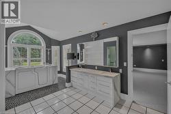 Spacious bathroom featuring a white walk-in tub with marble-look surround, an arched window with plantation shutters, a double vanity with stone countertops, and contrasting white tile flooring with p - 