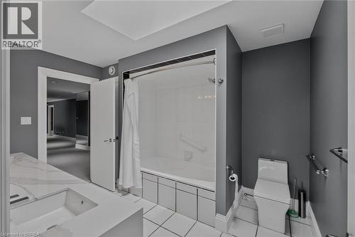 Bathroom featuring a built-in tub with a clear glass shower door, a spacious vanity with an integrated sink, white tile flooring, and dark gray walls - 44 St Andrew'S Drive, Brantford, ON - Indoor