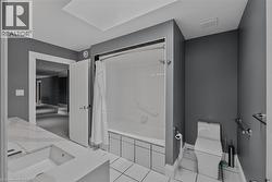 Bathroom featuring a built-in tub with a clear glass shower door, a spacious vanity with an integrated sink, white tile flooring, and dark gray walls - 