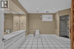 Bathroom featuring white square tile flooring with dark grout, a spacious dual vanity with white cabinetry and a light-toned countertop, a built-in toilet, a sauna with a wood door, and a glass-enclos - 