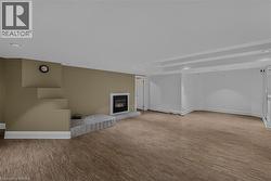 Spacious room featuring wood-finish flooring, a contemporary fireplace with a stone hearth, and a built-in architectural detail - 
