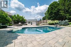 Expansive outdoor living area featuring a kidney-shaped swimming pool with integrated steps, surrounded by stone paver decking - 