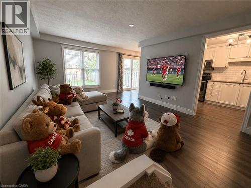 Open-concept living space featuring wood-finish flooring, a contemporary kitchen with white cabinetry and subway tile backsplash, a sliding glass door to a patio, and a large window with blinds - 41 Edgemere Drive, Cambridge, ON - Indoor Photo Showing Living Room