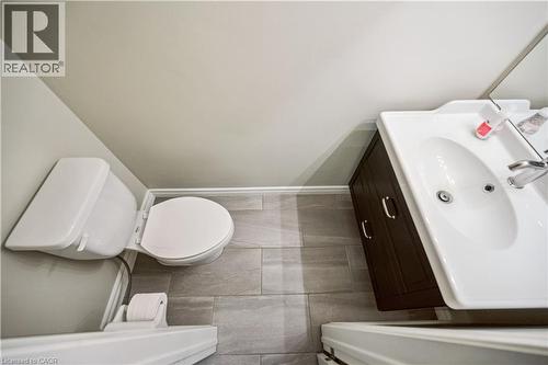 Powder room featuring a white single-sink vanity with a dark wood-finish cabinet and modern hardware, a white toilet, and gray plank-style floor tiling - 711 Johnston Park Avenue, Collingwood, ON - Indoor Photo Showing Bathroom