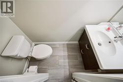 Powder room featuring a white single-sink vanity with a dark wood-finish cabinet and modern hardware, a white toilet, and gray plank-style floor tiling - 