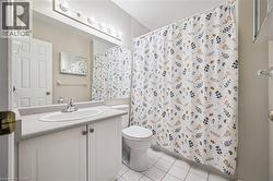 Bathroom featuring a white vanity with integrated sink, a large mirror, overhead vanity lighting, a toilet, and white tile flooring - 