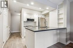 Kitchen featuring a central island with a sink and dark countertop, white shaker-style cabinetry, stainless steel appliances, a white subway tile backsplash, and recessed lighting - 