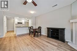 Open-concept living area with wood-finish flooring, a contemporary kitchen with white cabinetry and stainless steel appliances, and a breakfast bar - 