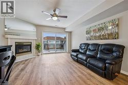 Living area featuring wood-finish flooring, a corner fireplace with a tile surround and mantel, a ceiling fan, and a sliding glass door opening to a balcony - 