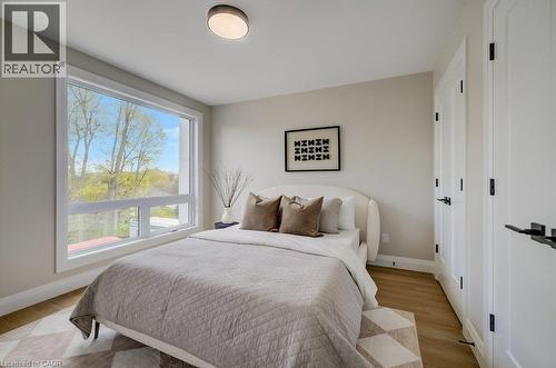 Bright room featuring a large rectangular window, wood-finish flooring, two white panel doors with black hardware, and a ceiling-mounted light fixture - 210 Heritage Drive Unit# Upper, Kitchener, ON - Indoor Photo Showing Bedroom