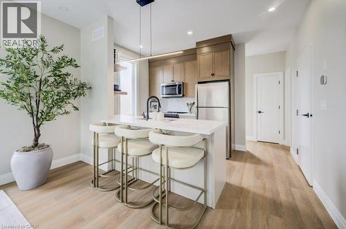 Modern kitchen featuring light wood-finish cabinetry, stainless steel appliances, a white countertop island with seating, and wood-finish flooring - 210 Heritage Drive Unit# Upper, Kitchener, ON - Indoor Photo Showing Kitchen