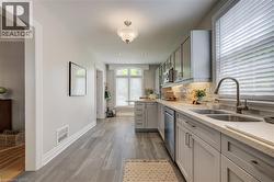 Galley kitchen featuring light gray cabinetry, stainless steel appliances, a double basin sink, light-toned countertops, and wood-finish flooring - 