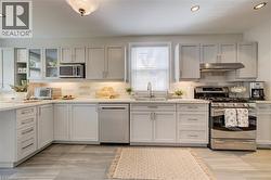 Contemporary kitchen featuring light gray cabinetry, stainless steel appliances, a white subway tile backsplash, and light-toned countertops - 