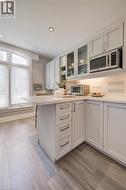 Kitchen featuring light gray cabinetry, built-in microwave, wood-finish tile flooring, recessed ceiling lighting, and an arched window - 