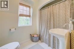 Bathroom featuring a pedestal sink, white tile flooring, and a window with a woven wood shade - 