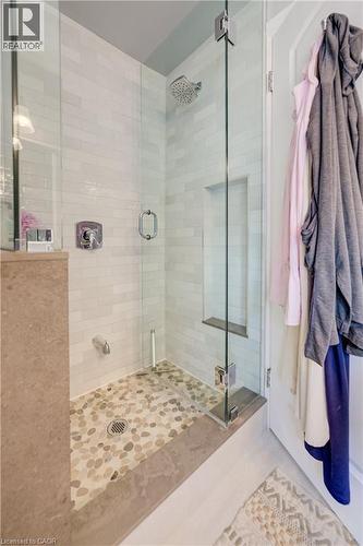 Walk-in shower featuring a frameless glass enclosure, pebble-stone flooring, subway tile walls, a built-in shower niche, and a chrome shower head with coordinating hardware - 314 Glasgow Street, Kitchener, ON - Indoor Photo Showing Bathroom