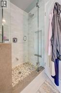 Walk-in shower featuring a frameless glass enclosure, pebble-stone flooring, subway tile walls, a built-in shower niche, and a chrome shower head with coordinating hardware - 