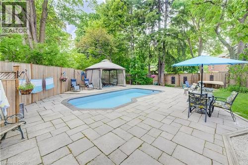 Outdoor entertainment area featuring a kidney-shaped pool, surrounding stone paver patio, full privacy fencing, and mature perimeter trees - 314 Glasgow Street, Kitchener, ON - Outdoor With In Ground Pool With Deck Patio Veranda With Backyard