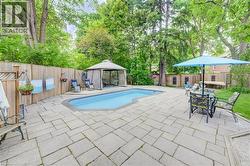 Outdoor entertainment area featuring a kidney-shaped pool, surrounding stone paver patio, full privacy fencing, and mature perimeter trees - 