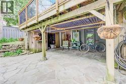 Stone patio featuring a covered seating area beneath a wood-frame deck with dark metal railings - 
