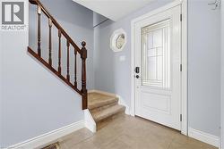 Entryway featuring a white door with frosted glass panels, tile flooring, and a hardwood staircase with carpeted treads - 