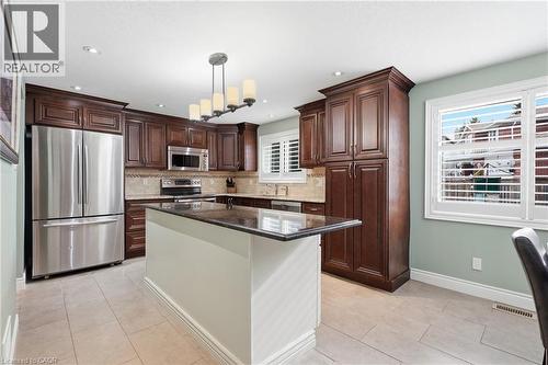 Kitchen featuring dark wood cabinetry, stainless steel appliances, a center island with a dark countertop, and light-toned tile flooring - 19 Alona Avenue, Cambridge, ON - Indoor Photo Showing Kitchen