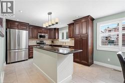 Kitchen featuring dark wood cabinetry, stainless steel appliances, a center island with a dark countertop, and light-toned tile flooring - 