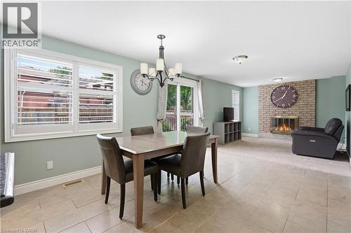 Dining area with tile flooring and a chandelier, opening to a living space featuring a brick fireplace - 19 Alona Avenue, Cambridge, ON - Indoor Photo Showing Dining Room With Fireplace