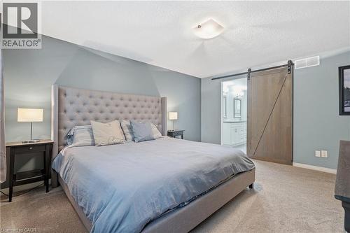 Carpeted bedroom with a light blue accent wall and a sliding barn door - 19 Alona Avenue, Cambridge, ON - Indoor Photo Showing Bedroom