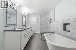 Contemporary bathroom featuring a freestanding soaking tub, a frameless glass shower enclosure with a built-in bench, and a double vanity with stone countertops - 