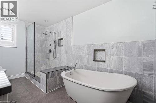 Freestanding soaking tub with chrome fixtures, a tiled shower enclosure featuring a built-in bench, dual shower heads, and recessed shelving - 19 Alona Avenue, Cambridge, ON - Indoor Photo Showing Bathroom