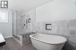 Freestanding soaking tub with chrome fixtures, a tiled shower enclosure featuring a built-in bench, dual shower heads, and recessed shelving - 