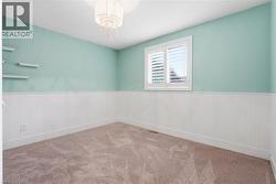 Room featuring paneled wainscoting, light-colored walls, carpet flooring, and a window with white shutters - 