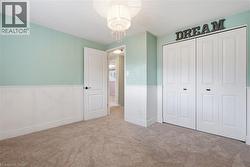 Bedroom featuring light green walls with white wainscoting, neutral carpet flooring, and a crystal chandelier - 