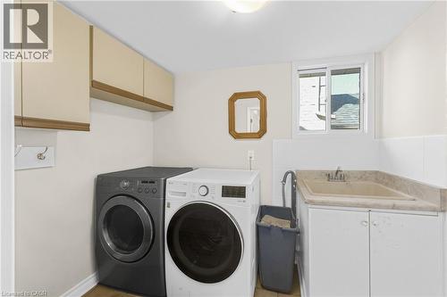 Dedicated laundry area featuring a utility sink with a stone-finish countertop, white base cabinetry, and a window - 123 Benn Drive, Cambridge, ON - Indoor Photo Showing Laundry Room