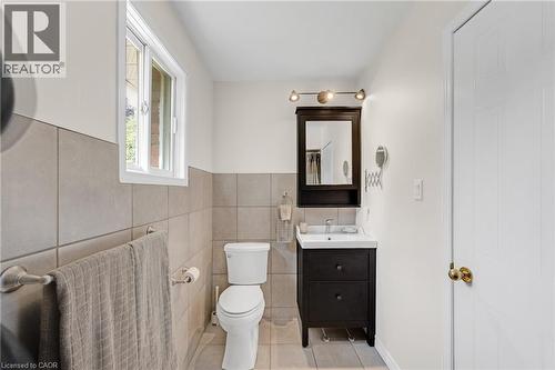 Bathroom featuring floor-to-ceiling tiling, a dark wood-finish vanity with an integrated sink, and a mirrored medicine cabinet with overhead lighting - 123 Benn Drive, Cambridge, ON - Indoor Photo Showing Bathroom
