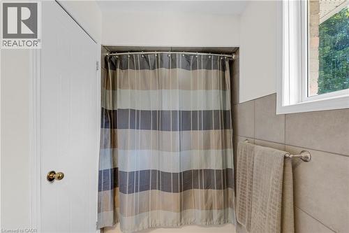Tiled shower surround with a window feature, complemented by a white paneled door with a brass knob - 123 Benn Drive, Cambridge, ON - Indoor Photo Showing Bathroom