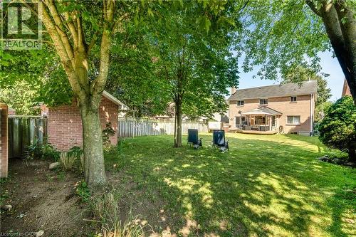 Expansive backyard featuring a lush lawn, mature trees, and a brick-sided home with a large wooden deck - 123 Benn Drive, Cambridge, ON - Outdoor With Deck Patio Veranda