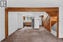 Living area featuring carpet flooring, natural wood beam entryway, and natural wood staircase - 
