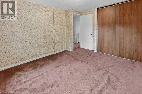 Carpeted room featuring a white door, sliding wood-finish closet doors, patterned wallpaper, and white baseboards - 125 Bonaventure Drive Unit# 50, Hamilton, ON - Indoor Photo Showing Other Room