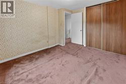 Carpeted room featuring a white door, sliding wood-finish closet doors, patterned wallpaper, and white baseboards - 