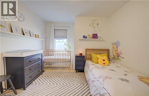 Light-filled room featuring a neutral color palette, wood-finish flooring with a chevron pattern rug, and a window with white curtains and a Roman shade - 290 William Street, Elmira, ON - Indoor Photo Showing Bedroom