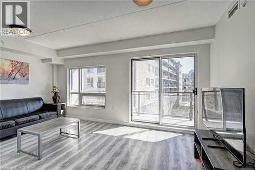 Living area featuring wood-finish flooring, white walls, and a sliding glass door opening to a balcony with metal railings - 275 Larch Street Unit# F209, Waterloo, ON - Indoor Photo Showing Living Room