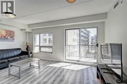 Living area featuring wood-finish flooring, white walls, and a sliding glass door opening to a balcony with metal railings - 