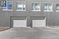 Gray brick facade with two white garage doors, asphalt driveway, and multiple upper-level windows - 