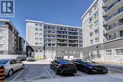 Modern multi-story building featuring stone-look and dark panel siding, individual balconies with glass railings, and a dedicated paved parking area - 