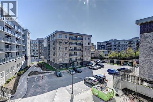 Modern multi-story buildings featuring stone and stucco exteriors, private balconies with glass railings, and a surface parking lot - 275 Larch Street Unit# F209, Waterloo, ON - Outdoor With Balcony