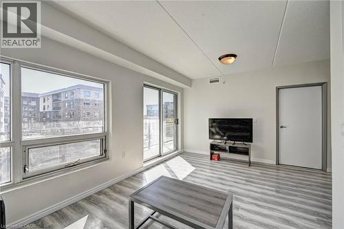 Spacious living area featuring light gray wood-finish flooring, white walls, and a large window with a sliding glass door - 275 Larch Street Unit# F209, Waterloo, ON - Indoor