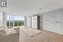 Spacious living area featuring floor-to-ceiling windows, tile flooring, a built-in wall unit, floating wall shelves, and an overhead lighting fixture - 
